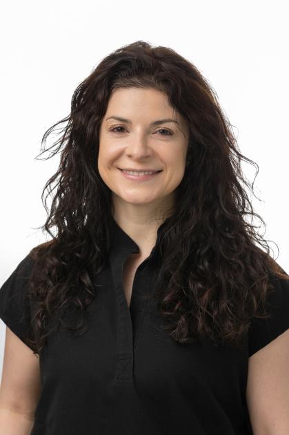 A person with long, curly dark hair is shown wearing a plain black shirt. The individual is positioned against a neutral background.